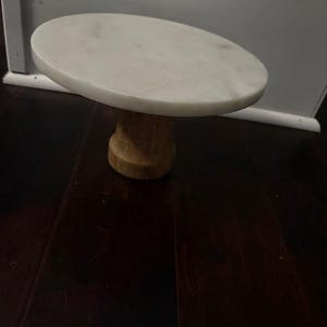 May include: White marble cake stand with a wooden base. The stand is round and has a smooth surface.