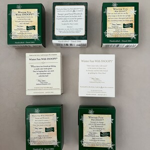 May include: A collection of green and white Hallmark "Winter Fun With Snoopy" miniature boxes. Each box features Snoopy and Woodstock in winter scenes, with text and dates. The boxes are handcrafted and dated from 2000 to 2011.
