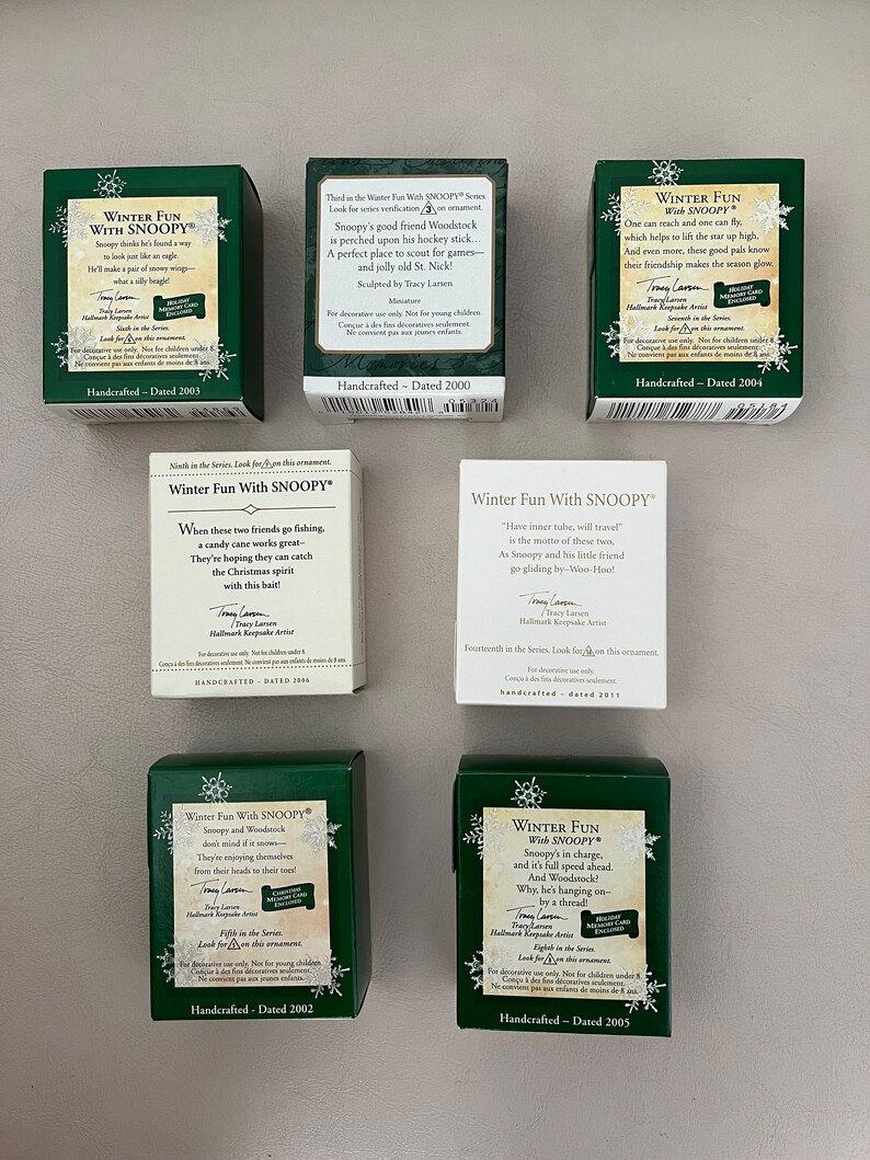 May include: A collection of green and white Hallmark "Winter Fun With Snoopy" miniature boxes. Each box features Snoopy and Woodstock in winter scenes, with text and dates. The boxes are handcrafted and dated from 2000 to 2011.