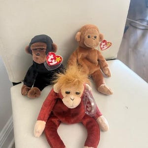 May include: Three plush monkey beanie babies. A brown monkey, a black monkey, and a red monkey. Each monkey has a white tag with the words "Ty" and a star.