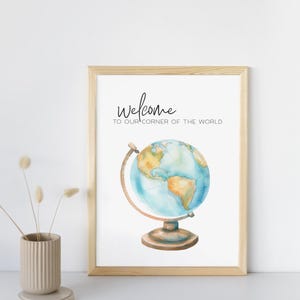 May include: A framed print featuring a watercolor globe illustration. The globe is in shades of blue and tan, with a wooden stand and frame. The text "welcome to our corner of the world" is written above the globe.