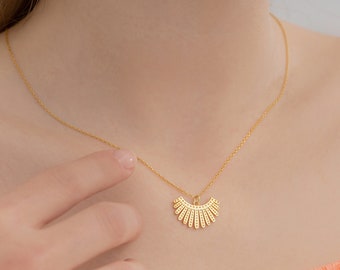 May include: A gold necklace with a delicate chain and a pendant shaped like a fan with a geometric design.