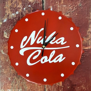 May include: A red clock in the shape of a bottle cap with the words "Nuka Cola" in white script. The clock has black hands and white dots around the edge. The clock is mounted on a weathered, reddish-brown wooden surface.