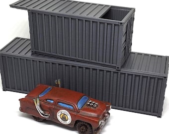 May include: Three gray miniature shipping containers, one with its lid open, stacked on top of each other. In front is a rusty red toy car with a circular emblem and exhaust pipes.
