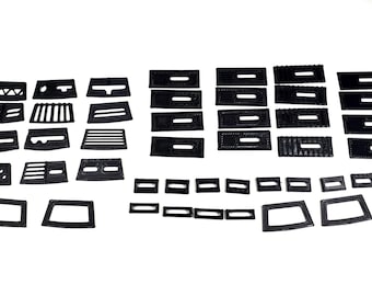 May include: A collection of various black, rectangular, and geometric-shaped objects. The assortment includes pieces with cut-out designs, ranging from small rectangles to larger, more complex shapes. The objects are arranged on a white surface.
