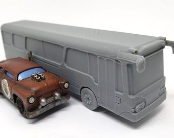 May include: A brown and gray toy car with a custom engine and a gray toy bus. The car has a weathered appearance with a circular emblem on the side. The bus has multiple windows and a detailed rear design.