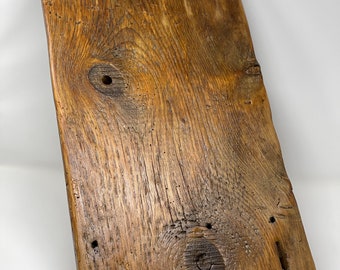 Könnte beinhalten: Ein rustikales Holztablett mit zwei schwarzen Metallgriffen. Das Tablett hat eine natürliche Holzoptik und eine einzigartige, unregelmäßige Form.