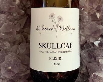 May include: A brown glass bottle with a black dropper top and a white label that reads "At Peace Wellness Skullcap (Scutellaria Lateriflora) Elixir 2 fl oz". The bottle is sitting on a bed of purple amethyst crystals.