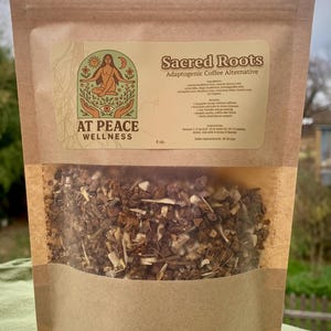 May include: A brown paper bag with a clear window, filled with a blend of dried herbs and roots. The label reads "Sacred Roots Adaptogenic Coffee Alternative" and features a logo with a woman and the words "At Peace Wellness". The bag contains 113 grams.