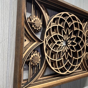 Puede incluir: Una obra de arte mural de madera en capas con un dise&ntilde;o geom&eacute;trico. La obra presenta un marco marr&oacute;n oscuro y patrones intrincados en tonos de marr&oacute;n y beige. El dise&ntilde;o incluye formas florales y circulares, creando un efecto tridimensional.