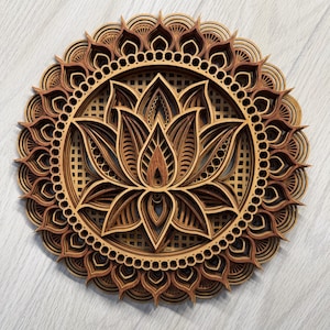 May include: A layered wooden mandala featuring a lotus flower design. The artwork is crafted from various shades of brown wood, creating a three-dimensional effect. The mandala has a circular shape with intricate details and a lattice background.