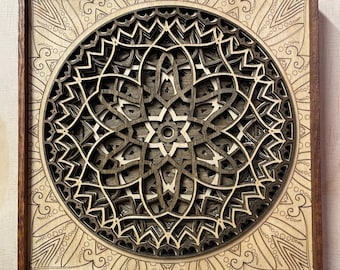 Puede incluir: Una pieza de arte mural cuadrada de madera con un diseño de mandala circular de varias capas. La obra consiste en paneles de madera cortados con láser y superpuestos en tonos marrones claros y oscuros, dentro de un marco de madera oscura.
