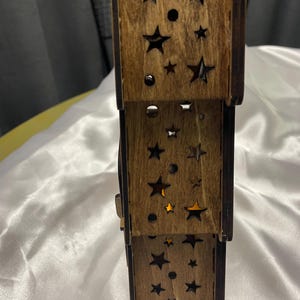 May include: A wooden tiered candle holder with a star and circle cut-out design. The candle holder is made of natural wood and has a rustic look.
