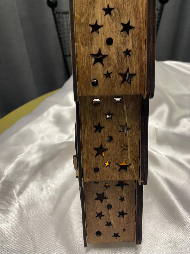 May include: A wooden tiered candle holder with a star and circle cut-out design. The candle holder is made of natural wood and has a rustic look.