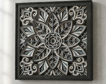 Puede incluir: Una pieza de arte mural cuadrada que presenta un diseño de mandala multicapa con intrincados pétalos en forma de hoja y patrones en espiral. La obra está compuesta por capas apiladas en tonos gris carbón, gris claro y blanco, en un marco negro.