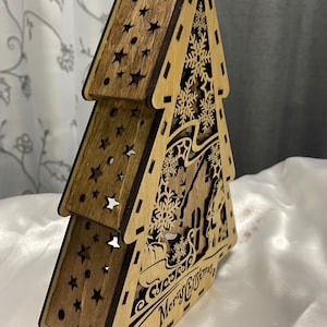 May include: A wooden Christmas tree cutout with a brown stain. The tree is layered and features snowflakes, stars, and the text "Season's Greetings Merry Christmas".