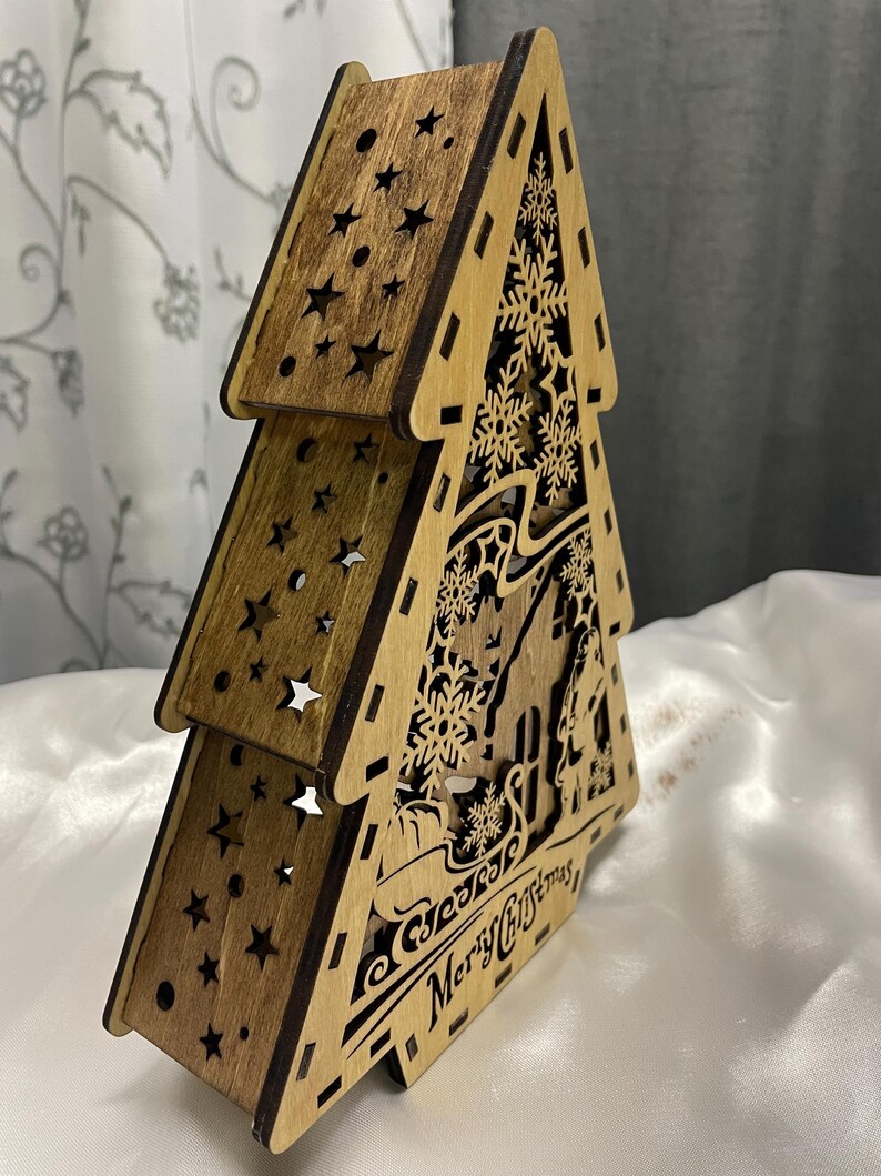 May include: A wooden Christmas tree cutout with a brown stain. The tree is layered and features snowflakes, stars, and the text "Season's Greetings Merry Christmas".