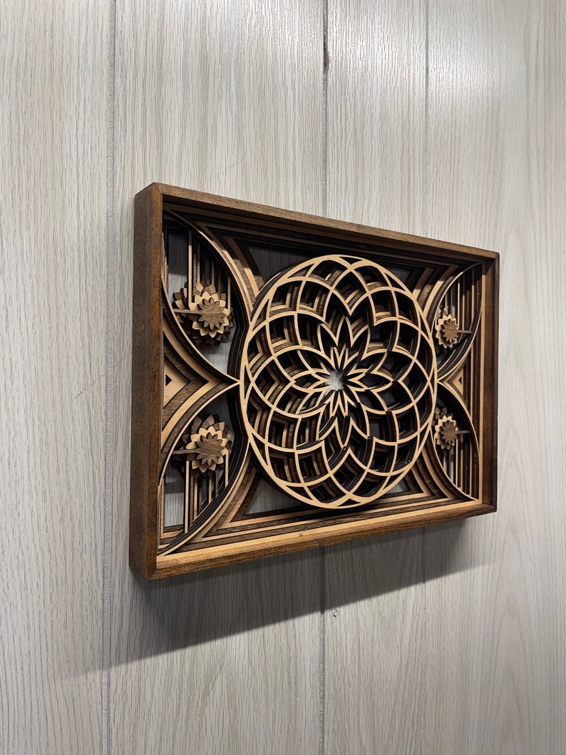 Puede incluir: Una pieza de arte mural de madera en capas con un dise&ntilde;o floral geom&eacute;trico. La obra de arte est&aacute; construida a partir de m&uacute;ltiples capas de madera, creando un efecto tridimensional. El marco es de color marr&oacute;n oscuro y las capas interiores son de un tono de madera m&aacute;s claro.