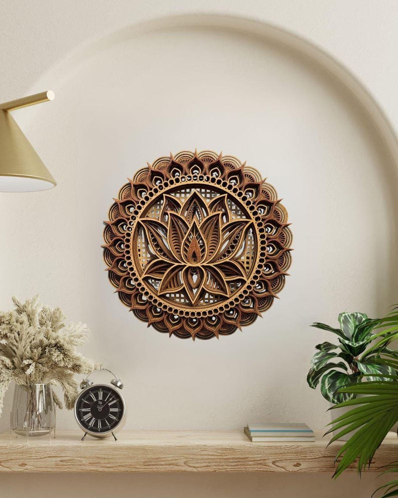 A layered wooden lotus mandala with light and dark wood tones hangs on a light beige wall above a wooden shelf with a clock and plants.