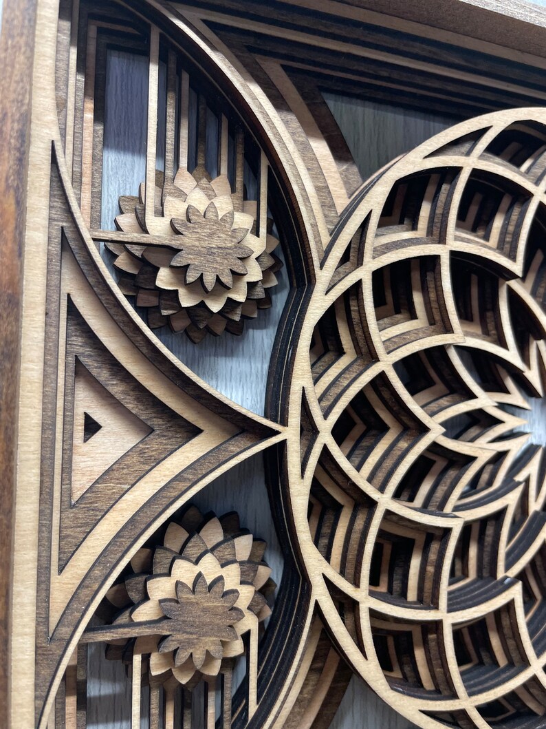 Puede incluir: Una obra de arte de madera en capas con intrincados dise&ntilde;os geom&eacute;tricos. La obra presenta una combinaci&oacute;n de madera marr&oacute;n oscura y clara, creando un efecto tridimensional. El dise&ntilde;o incluye formas florales y geom&eacute;tricas, con un enfoque en patrones en capas y cortes de precisi&oacute;n.