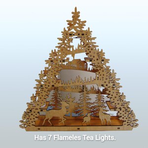 A laser-cut wooden Christmas decoration, shaped like a tree, shows a layered winter scene with deer, trees, and a house, with seven flameless tea lights.