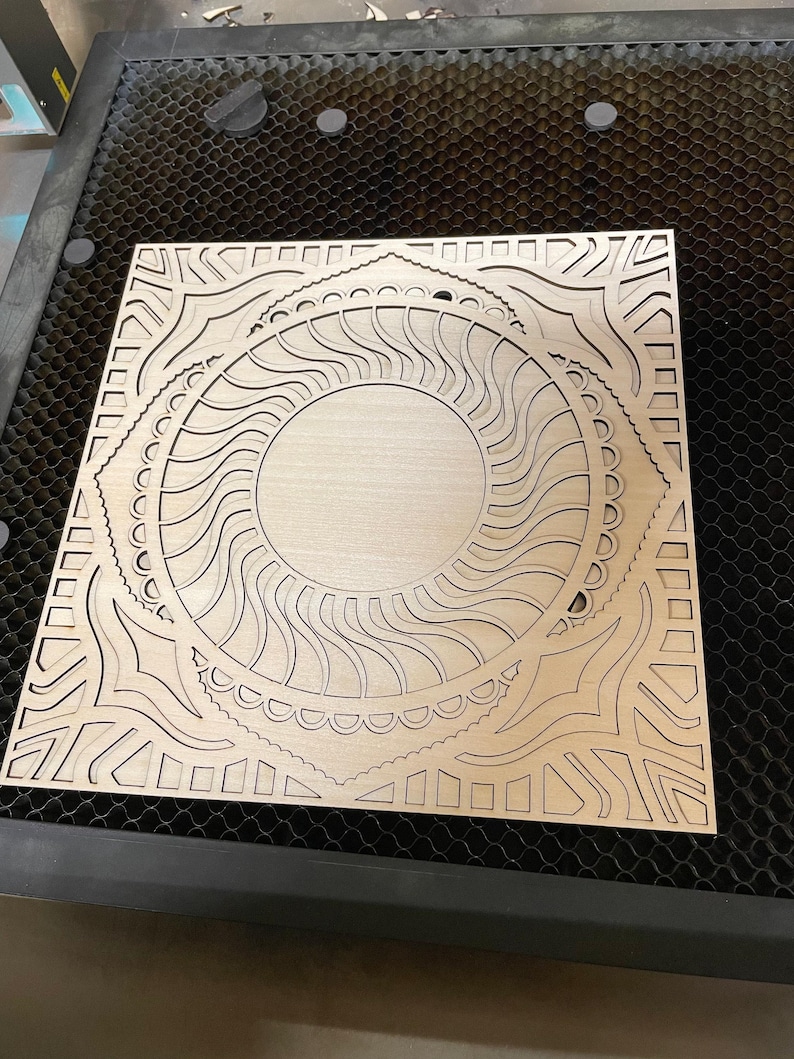 Close-up view of an intricately laser-cut light wood square panel featuring circular mandala and geometric patterns.