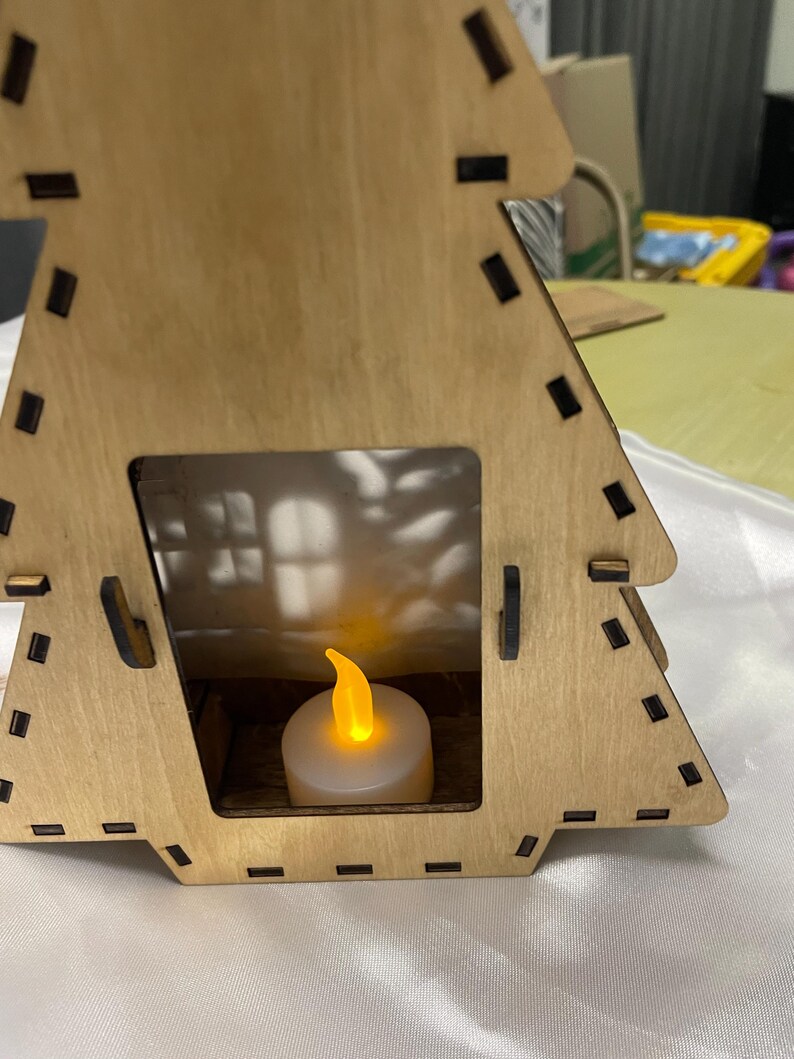 May include: A wooden Christmas tree shaped candle holder with a small white candle inside. The candle is lit and the flame is visible.