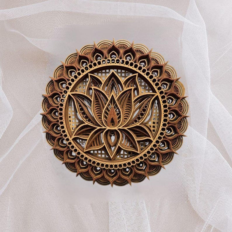 A layered wooden lotus mandala with light and dark wood tones is centered on a sheer white fabric background.