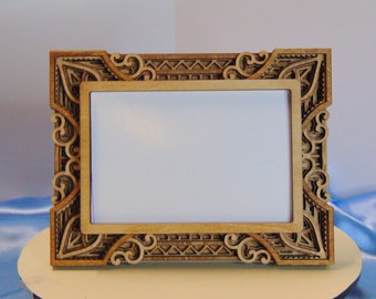 May include: A decorative wooden picture frame with intricate, layered geometric and scrollwork designs. The frame is made of light-colored wood and has a rectangular opening for a photo or artwork.