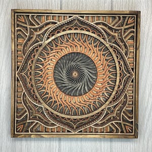 A square multi-layered wooden mandala wall art piece featuring geometric and swirling patterns in various wood tones.