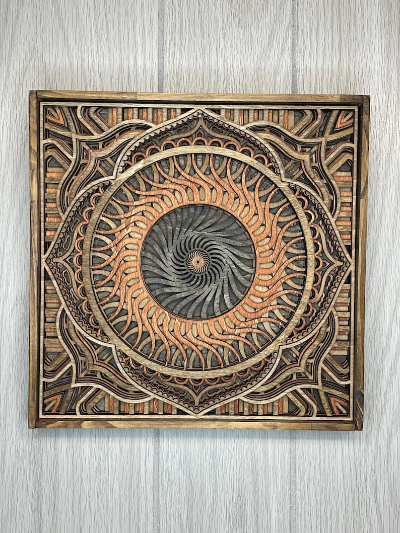 A square multi-layered wooden mandala wall art piece featuring geometric and swirling patterns in various wood tones.