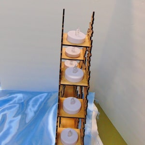 A side view of the laser-cut wooden Christmas decoration shows seven flameless tea lights placed on individual shelves within the structure.