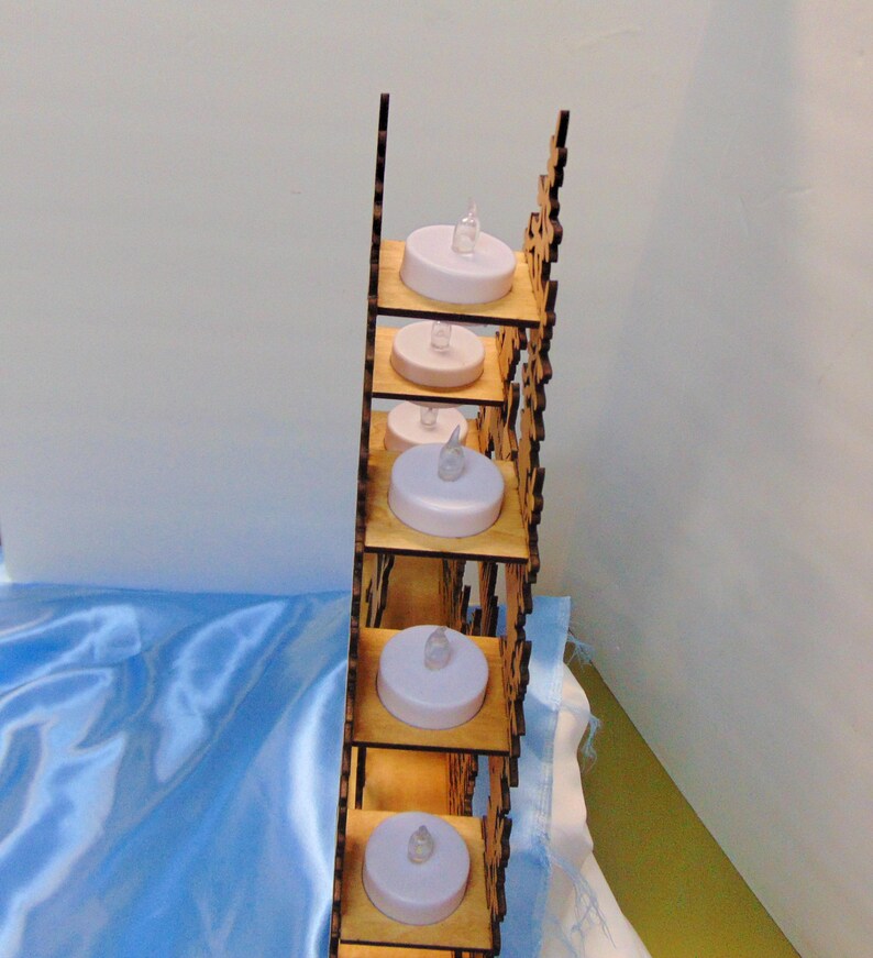 A side view of the laser-cut wooden Christmas decoration shows seven flameless tea lights placed on individual shelves within the structure.