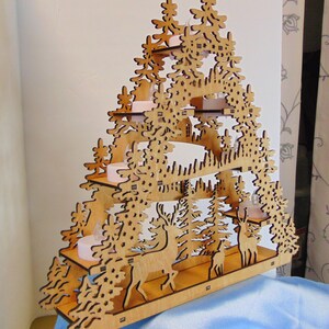 K&ouml;nnte beinhalten: Ein h&ouml;lzerner Weihnachtsbaumschmuck mit einem mehrschichtigen Design, das eine Waldszene mit Hirschen und B&auml;umen zeigt. Der Baum hat vier Ebenen mit Platz f&uuml;r Kerzen oder Lichter.