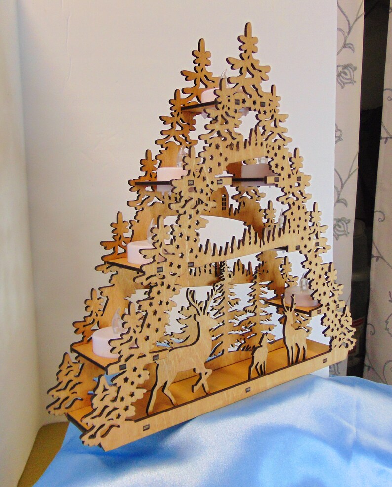 K&ouml;nnte beinhalten: Ein h&ouml;lzerner Weihnachtsbaumschmuck mit einem mehrschichtigen Design, das eine Waldszene mit Hirschen und B&auml;umen zeigt. Der Baum hat vier Ebenen mit Platz f&uuml;r Kerzen oder Lichter.