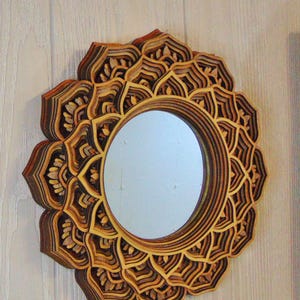 A round wooden wall mirror with layered mandala flower petals hanging on a textured wall.