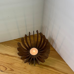K&ouml;nnte beinhalten: Ein Kerzenhalter aus Holz in Form einer Blume mit einer brennenden Kerze in der Mitte.