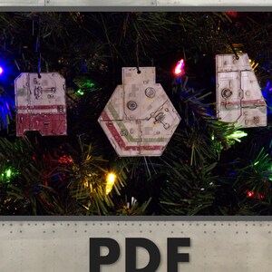 May include: A Christmas tree decorated with three paper ornaments shaped like spaceships. The ornaments are white, green, and red with black details. The text "PDF Template" is printed below the tree.