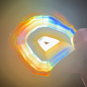 May include: A close-up of a colourful agate slice with a rainbow of colours, including red, orange, yellow, green, blue, and purple. The agate is translucent and has a smooth, polished surface.