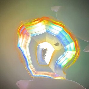 May include: A close-up of a colourful agate geode with a white interior and rainbow-coloured bands. The geode is illuminated from behind, creating a glowing effect.