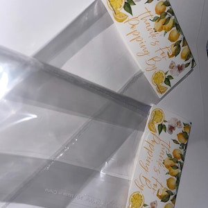 Może przedstawiać: Dwie przezroczyste plastikowe torebki na smakołyki z ozdobną kartą nagłówkową w cytryny i białe kwiaty. Napis "Thanks for Popping By" jest wydrukowany złotą czcionką przypominającą pismo odręczne na górnej części torebki.
