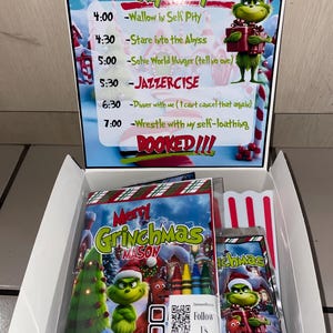 Może przedstawiać: Świąteczne pudełko upominkowe z motywem Grincha. Pudełko zawiera notatnik, kredki i torebkę popcornu. Na okładce notatnika widnieje napis "Merry Grinchmas MASON". Pudełko zawiera r&oacute;wnież harmonogram z zabawnymi zajęciami.