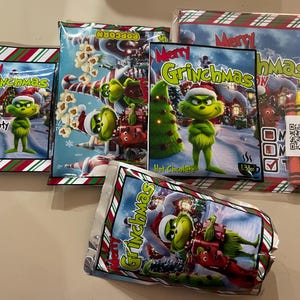 Może przedstawiać: Asortyment smakołyk&oacute;w i aktywności o tematyce Grinchmas. Zawiera popcorn, gorącą czekoladę i zestaw kredek. Opakowanie przedstawia postać Grincha, choinki i napis "Merry Grinchmas".