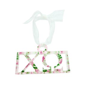 May include: A rectangular Christmas ornament with a white ribbon. The ornament features the Greek letters ΧΩΩ in a cut-out design. The letters are decorated with a pattern of pink and green Christmas trees on a white background.