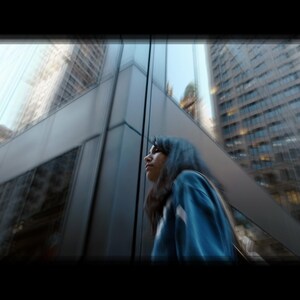 Puede incluir: Una mujer con el pelo azul se encuentra frente a un gran edificio de cristal, mirando hacia arriba y hacia la derecha.