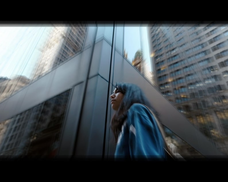 Puede incluir: Una mujer con el pelo azul se encuentra frente a un gran edificio de cristal, mirando hacia arriba y hacia la derecha.