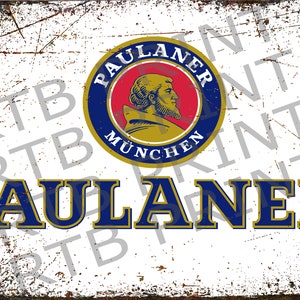 Op de afbeelding: Een vintage-stijl metalen bord met een blauw en gouden logo voor Paulaner M&uuml;nchen bier. Het logo toont een monnikshoofd en de tekst "Paulaner M&uuml;nchen". Het bord bevat ook de tekst "Paulaner" in grote, blauwe letters.