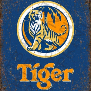 Op de afbeelding: Een vintage metalen bord met een verweerde blauwe achtergrond en een roestige oranje rand. Het bord heeft een cirkelvormig logo met een witte omtrek en een gele tijger erin. De tijger zit op een gele palmboom met een gele zon erachter. Het woord "Tiger" staat in grote oranje letters onder het logo.