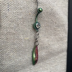May include: A green and iridescent belly button ring with a clear gem and a dangling charm shaped like a leaf.