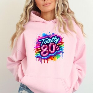 May include: Pink hoodie with a graphic print of a neon sign that says "Totally 80's" with rainbow colored paint splatters.
